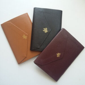 Re-usable Pocket Book - 11 Nov 2023 Three faux leather pocket notebooks with triangular flaps. They are tan, black, and maroon, with a little gold tooling on the flap.